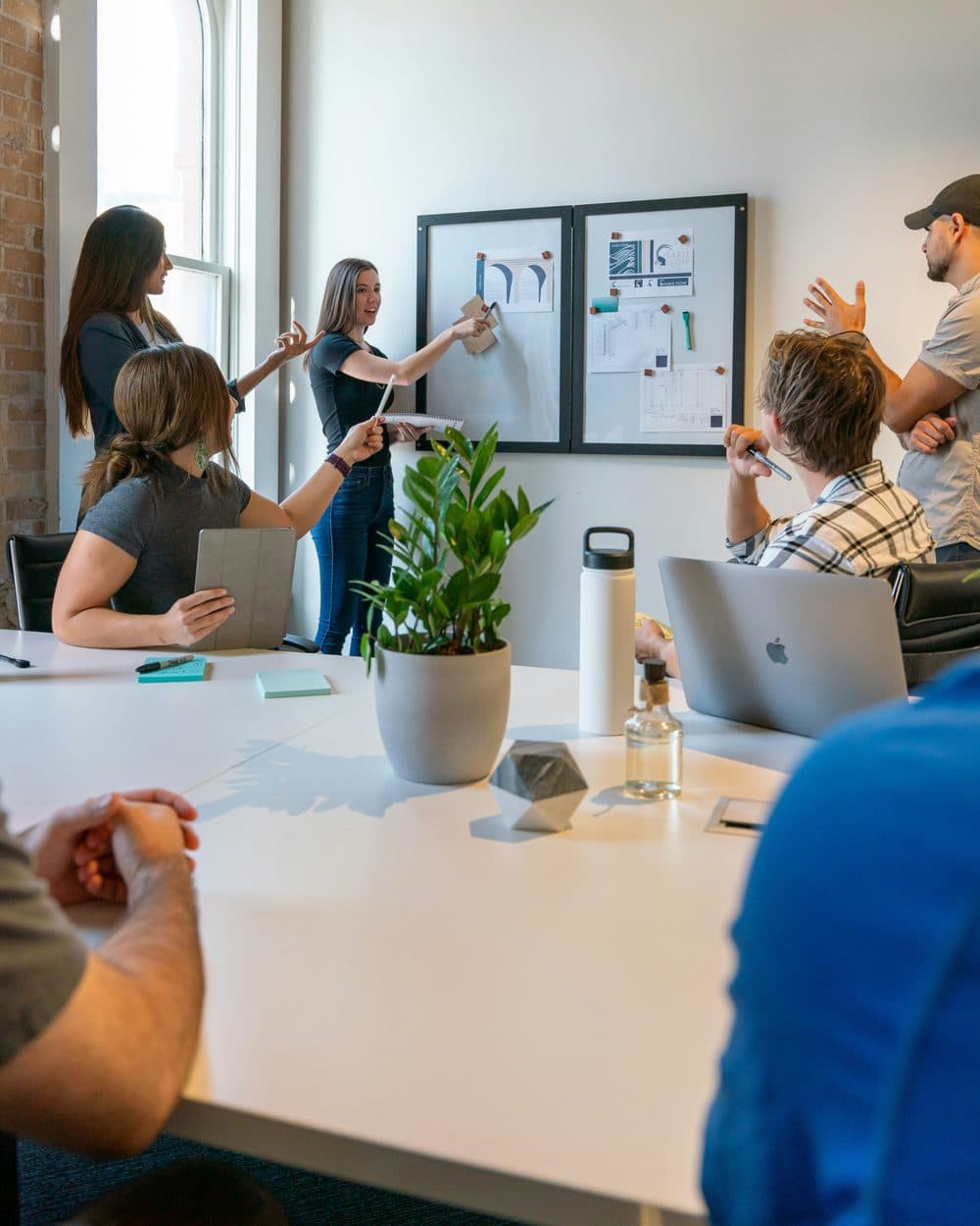 A team gathered around a pinboard, one person presenting while colleagues weigh in